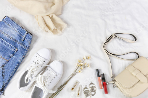 Blue jeans and jacket, bag and white sneakers on white bedsheets. Women's stylish summer or spring outfit. Trendy fashion clothes. Flat lay, top view.