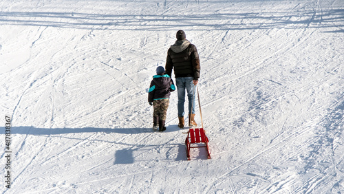 Man with his son and a sled climbing up the slope in the Carpathians in winter, Romania photo