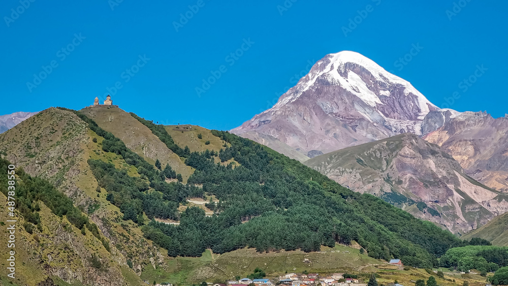 Distant view on Gergeti Trinity Church in Stepansminda, Georgia. The church is located the Greater Caucasian Mountain Range. Clear sky above the snow-capped Mount Kazbegi in the back. Sunrise, sunset