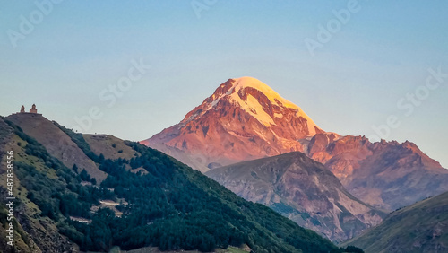 Distant view on Gergeti Trinity Church in Stepansminda  Georgia. The church is located the Greater Caucasian Mountain Range. Clear sky above the snow-capped Mount Kazbegi in the back. Sunrise  sunset