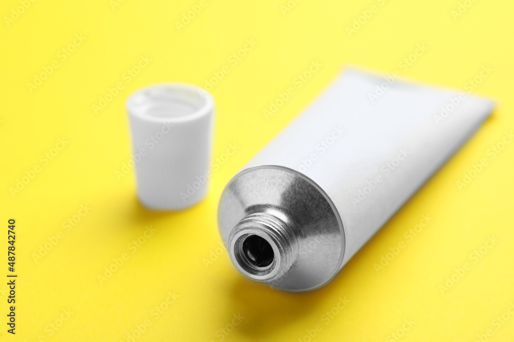 Open white tube of ointment on yellow background, closeup Open white tube of ointment on yellow background, closeup