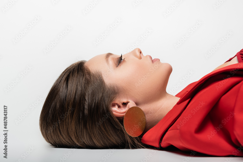 side view of trendy young woman in red blazer lying on grey. side view of trendy young woman in red blazer lying on grey.