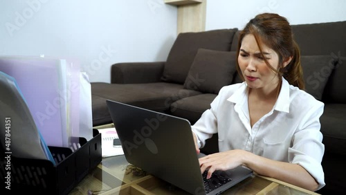 Young Asian woman sitting on the floor and using laptop for working in living room at home frowning and getting moody from working seriously.