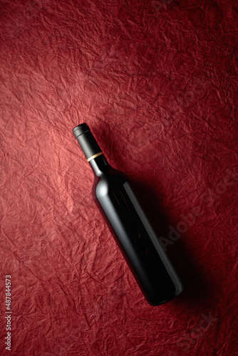 Bottle of red wine on a crumpled red paper background.