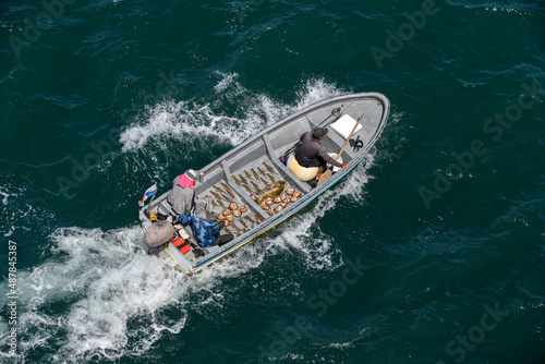 Small fishing boat with fishermen sailing at sea. Fish, shells, lobsters in boat. Top view. © Alexey Seafarer