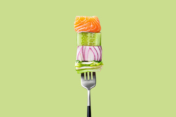 Close-up of fork with food on it: delicious fillet salmon, cucumber, onion, green salad on green background. Concept of healthy diet and clean eating, balanced nutrition space for text