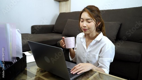 Young sitting on the floor drinking coffee and working in living room at home.