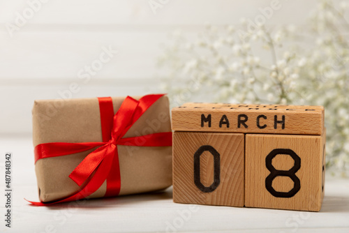 International Women's Day. Beautiful card for March 8. A bouquet of delicate gypsophila flowers with a wooden calendar and a gift box on a white textured wood. Holiday concept.Copy space.