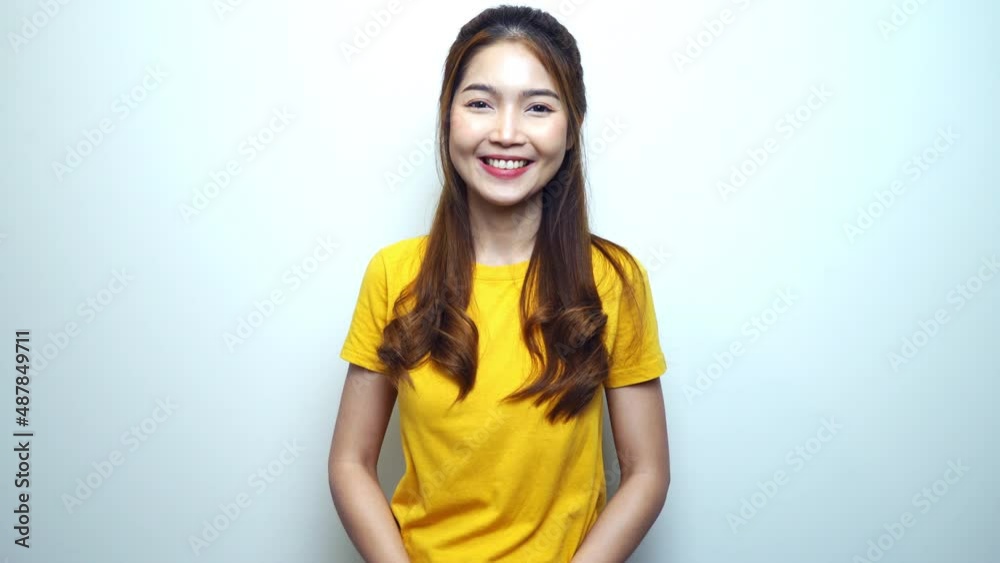 Happy young Asian woman in yellow t-shirt looking to camera and smiling joyfully, white background. Happy young Asian woman in yellow t-shirt looking to camera and smiling joyfully, white background.