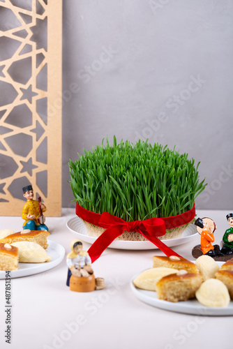 Green fresh semeni sabzi wheat grass in white plate with traditional Azerbaijani pastry shekerbura and pakhlava with wooden shebeke pattern, Novruz spring equinox celebration in Azerbaijan