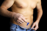 Muscular man in unbuttoned jeans with naked torso standing with straight razor in hand. Hair removal and  depilation concept, male health and intimate shaving