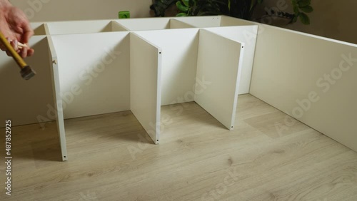 Man's hands hammering dowels into the holes in the shelves. In the background is a green flower. Assembling furniture at home with his own hands photo