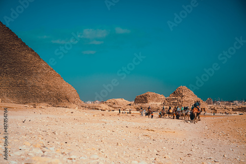 Tourists riding on camels in a convoy around the great pyramids of giza. Amazing view on a sunny winter day