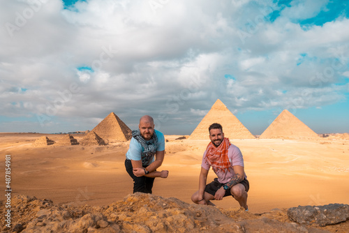 Two men travelers posing in front of the great pyramids of giza in cairo egypt. Traveling egypt during the winter, cold winter overcast day.