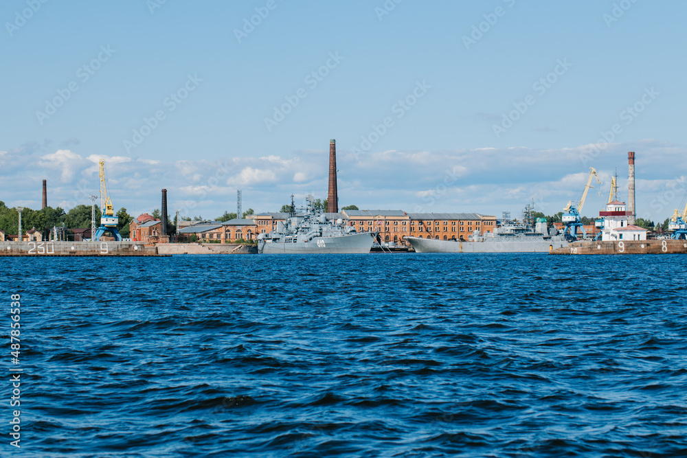 View from the water to the coastline of Kronstadt,where there are warships and ships,sea cranes on the platform,blue water and big waves.Russia,Kronstadt,31.07.2021
