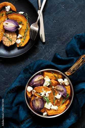 Pan with roasted pumpkin,onion,garlic,thyme and rosemary on dark blue background. Rustic food photography.  Low key.Top view with copy space.