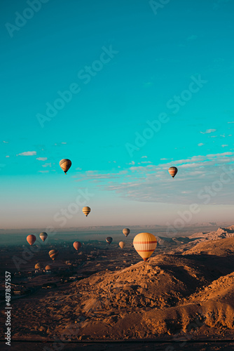Amazing vertical shot of dozens of hot air balloons flying around the luxor egypt area. Desert orange area early in the morning. Bright blue sky