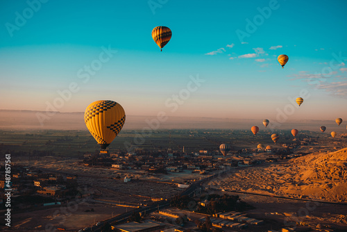 Amazing vertical shot of dozens of hot air balloons flying around the luxor egypt area. Desert orange area early in the morning. Bright blue sky