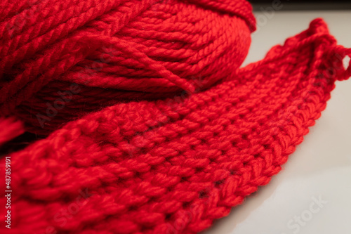 Close-up of an unknitted piece of wool next to a ball of yarn. Red wool yarn