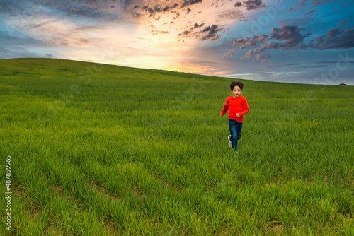 6 Year Old Boy Running Through A Green Meadow With A Spectacular Sky And A Nice Horizon. Image With Copy Space. Freedom Concept © Nanci