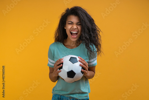 Studio image of excited soccer fan girl holding ball in hands looking at the camera with amazed face expression, celebrating her favorite team victory © wpadington