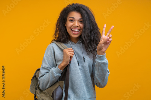 Studio portrait of casually dressed happy smiling cheerful african american student showing v-sign gesture, isolated over bright colored yellow background photo