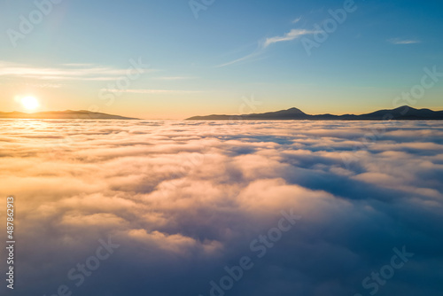 Aerial view of vibrant yellow sunrise over white dense clouds and distant mountains on horizon