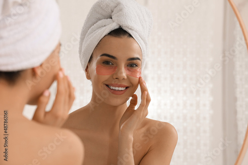 Beautiful young woman with under eye patches near mirror at home