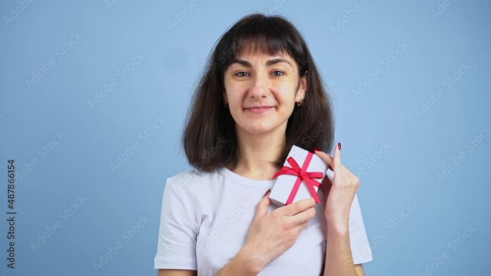 Beautiful smiling woman holding gift box in hand on blue wall background. Girl is happy with present Beautiful smiling woman holding gift box in hand on blue wall background. Girl is happy with present