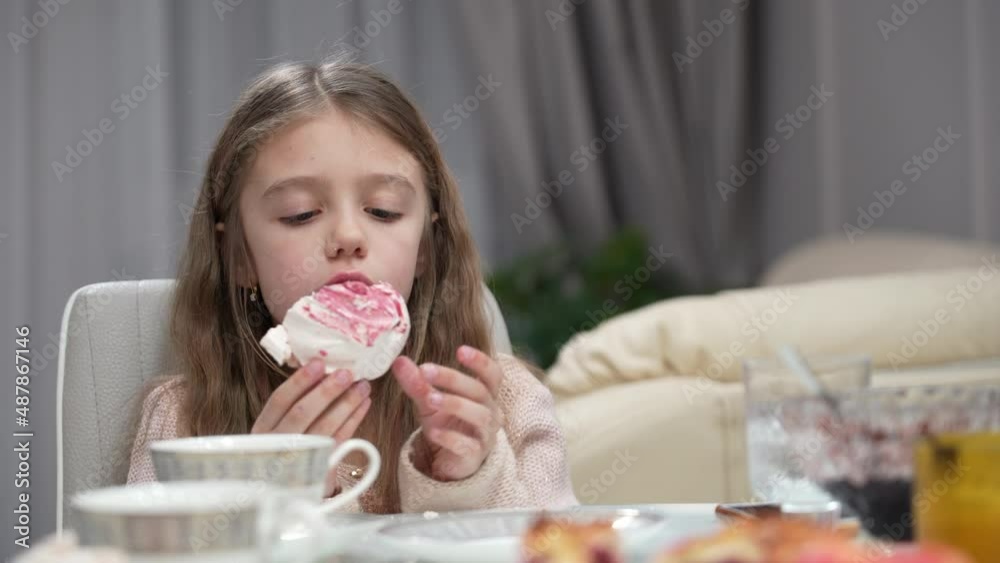 Nice little girl eats meringue. Cute little girl eating big meringue in light kitchen Nice little girl eats meringue. Cute little girl eating big meringue in light kitchen