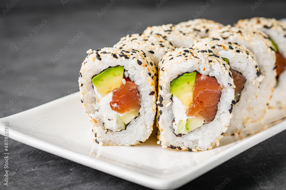 appetizing california sushi roll with cheese avocado cucumber and salmon in sesame seeds on a black stone plate appetizing california sushi roll with cheese avocado cucumber and salmon in sesame seeds on a black stone plate