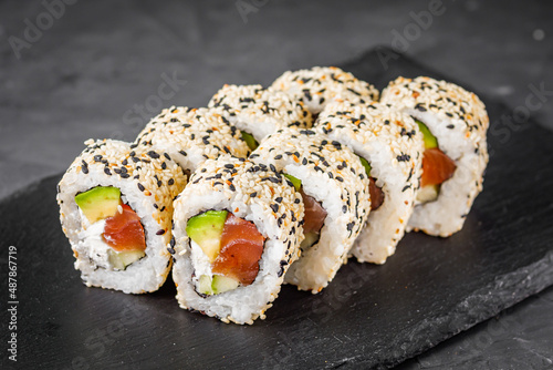 appetizing california sushi roll with cheese avocado cucumber and salmon in sesame seeds on a black stone plate