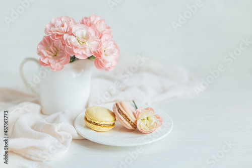 Two tasty French macarons and a jar with pink carnation flowers on a white background.
