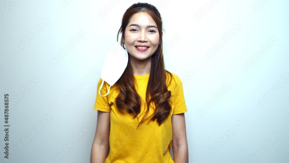 Young Asian woman taking off medical mask one side, looking at camera and smiling when corona virus pandemic is over, white background. Young Asian woman taking off medical mask one side, looking at camera and smiling when corona virus pandemic is over, white background.