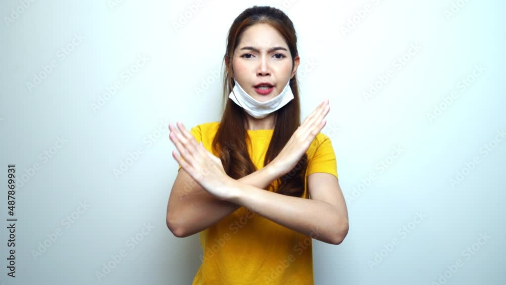 Young Asian woman wearing medical mask wrongly, saying no and showing crossing hands gesture, white background. Young Asian woman wearing medical mask wrongly, saying no and showing crossing hands gesture, white background.