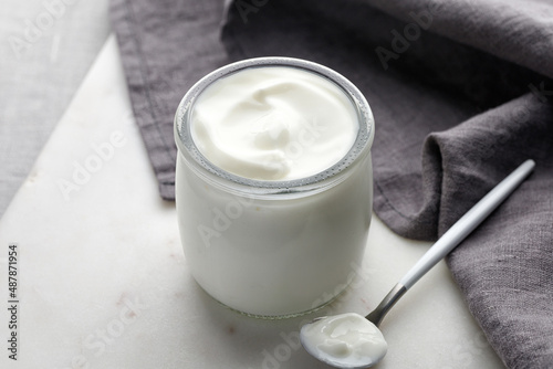 Empty white nature yogurt in glass jar on marble board with spoon and grey napkin. Simple and minimalistic.