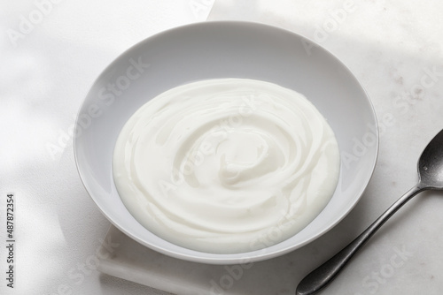 Greek yogurt in white bowl. Close up, top view. Tasty yogurt on marble backgound. Wave of white yogurt