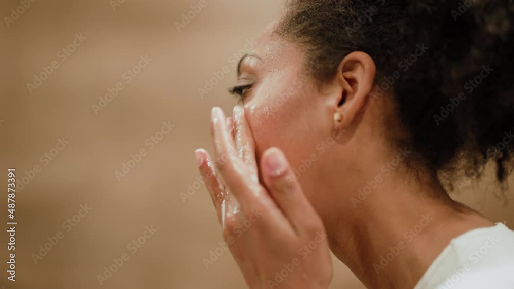 African woman washing with facial cleanser in the bathroom at home