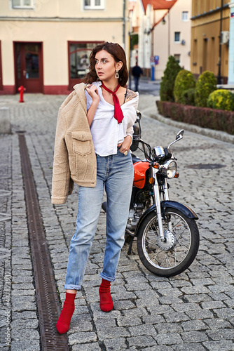 Obraz na płótnie Young beautiful woman in red knitted fabric block heel sock shoes, blue denim jeans pants and teddy jacket coat posing near a motorcycle on a street w salonie