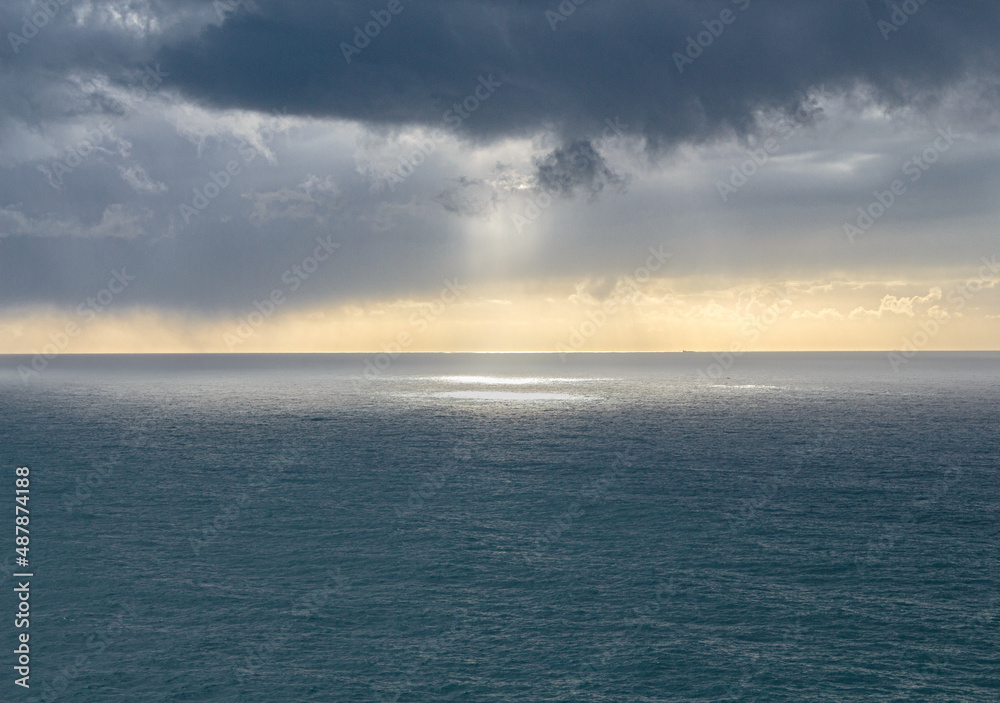 The sun breaking through the clouds over the ocean. Light blur in the sea. Gentle clouds over the sea. The horizon is bathed in light