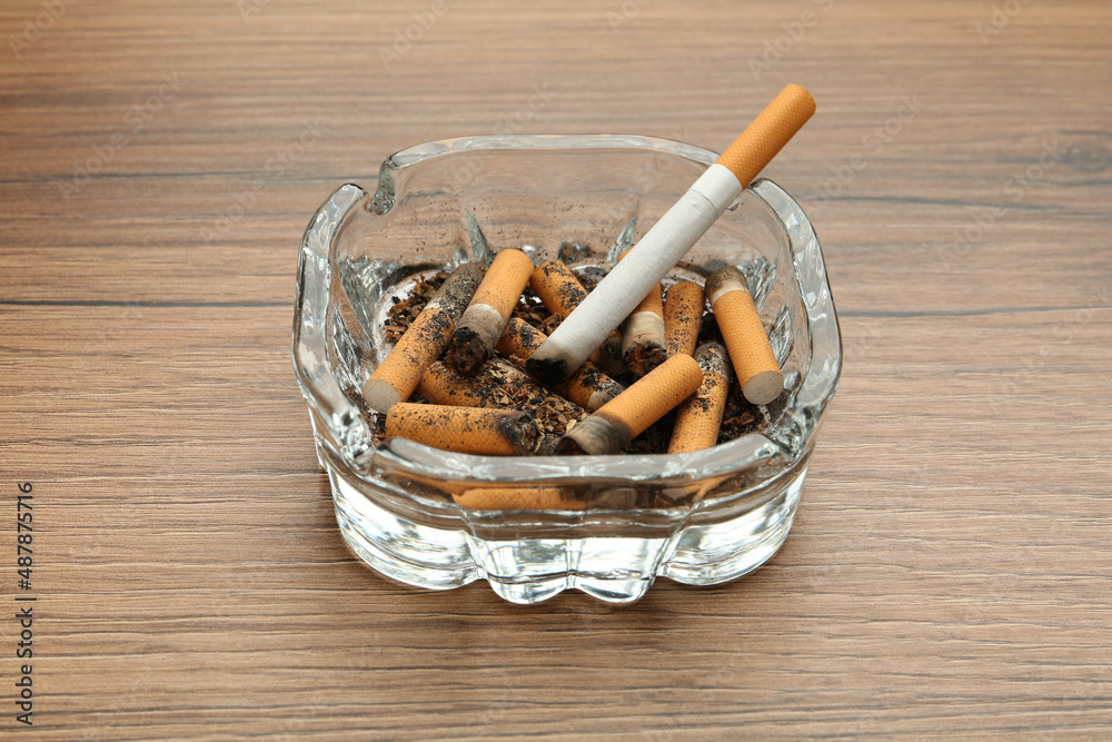 Glass ashtray with cigarette stubs on wooden table Glass ashtray with cigarette stubs on wooden table
