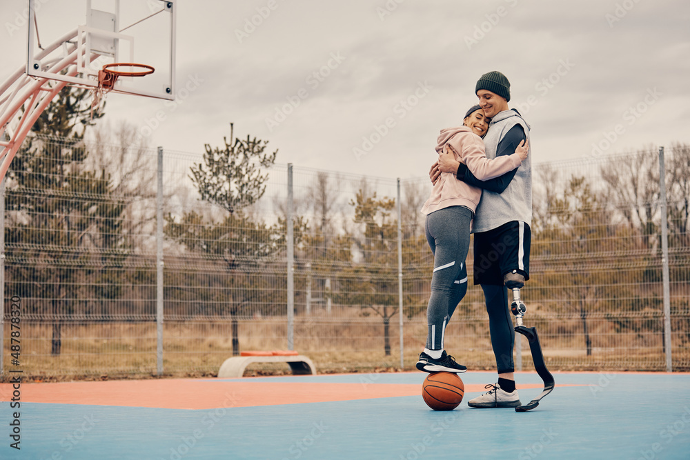 Φωτογραφία Happy athlete with artificial leg embraces his girlfriend while she is standing on a basketball on outdoors sports court