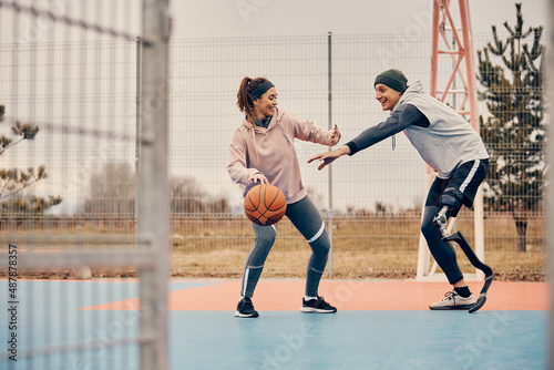 Happy woman and her boyfriend with leg disability playing basketball outdoors,