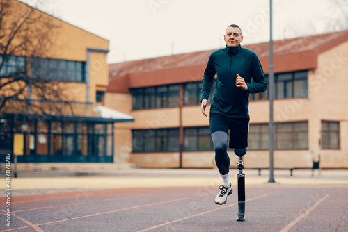 Male runner with prosthetic leg running during practice on outdoor sports field.