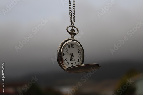 Vintage pocket watch hanging against cloudy sky