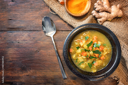Fototapeta Naklejka Na Ścianę i Meble -  Vegetable soup with curry, turmeric and ginger in a dark bowl on a rustic wooden table, copy space, high angle view from above