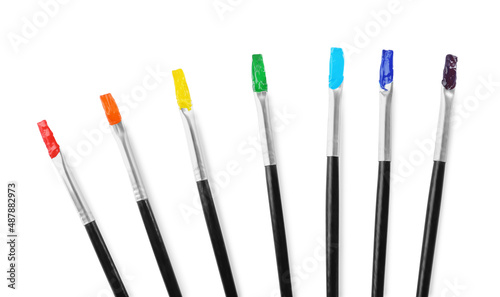 Brushes with colorful paints on white background, top view