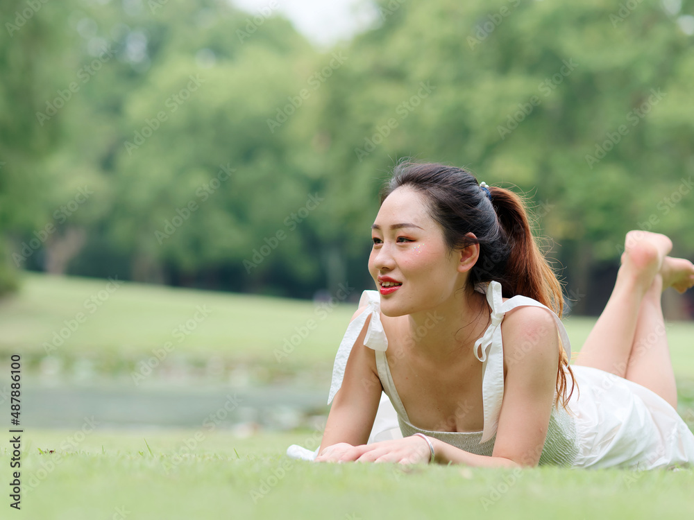 Portrait of young Asian woman lying on grass field with barefoot in forest park, beautiful Chinese girl in white dress enjoy her carefree time in sunny summer day, full length shot. Portrait of young Asian woman lying on grass field with barefoot in forest park, beautiful Chinese girl in white dress enjoy her carefree time in sunny summer day, full length shot.