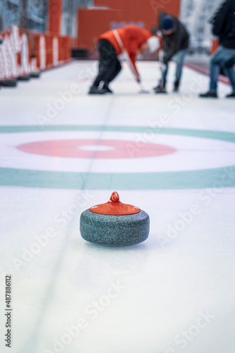 Granite projectile for curling on ice against background of playing athletes, selective focus