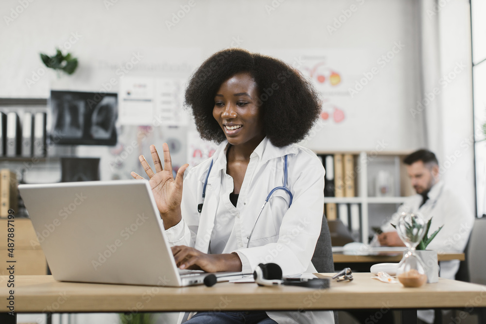 African american female doctor smiling and waving during video call with patient on laptop. Online consultation, medicine and technology concept. African american female doctor smiling and waving during video call with patient on laptop. Online consultation, medicine and technology concept.